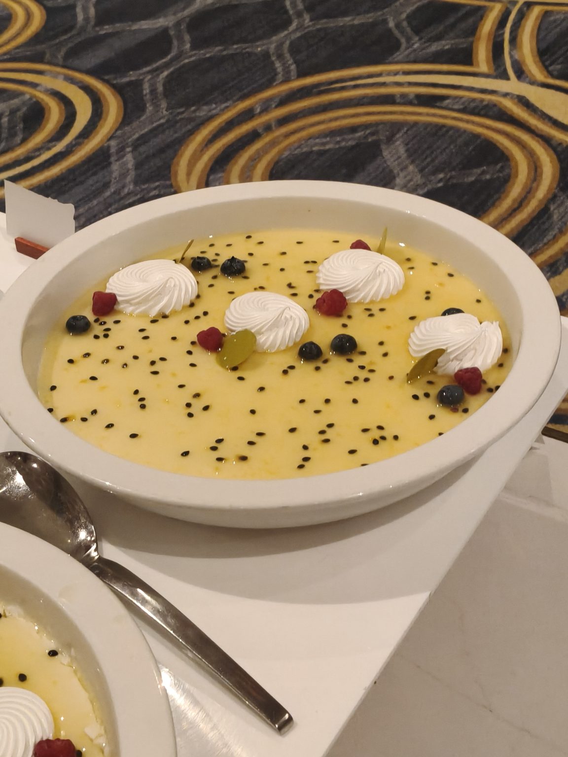 Creamy passion fruit dessert topped with whipped cream, berries, and fruit pieces.