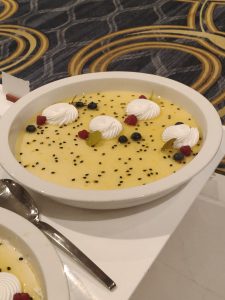 Creamy passion fruit dessert topped with whipped cream, berries, and fruit pieces.
