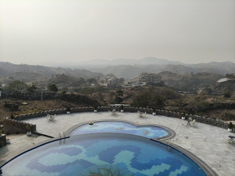 A swimming pool with a mountain view, surrounded by trees and outdoor seating.