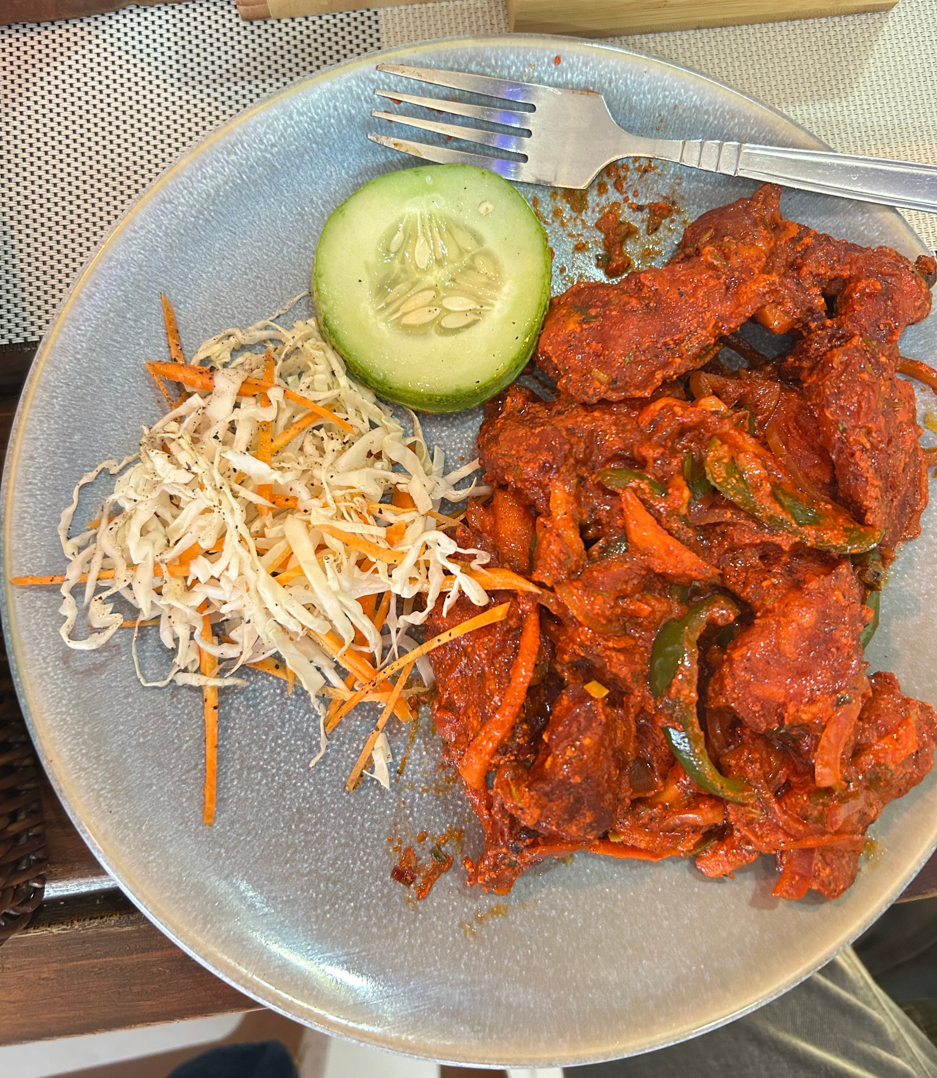A round blue plate holds a serving of bright red, spicy chicken pieces, which are garnished with thinly sliced green bell peppers.