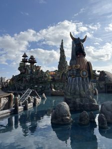A large horned stone statue beside a clear pond at a theme park.
