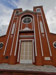 
Large orange church with twin clock towers under a partly cloudy sky.