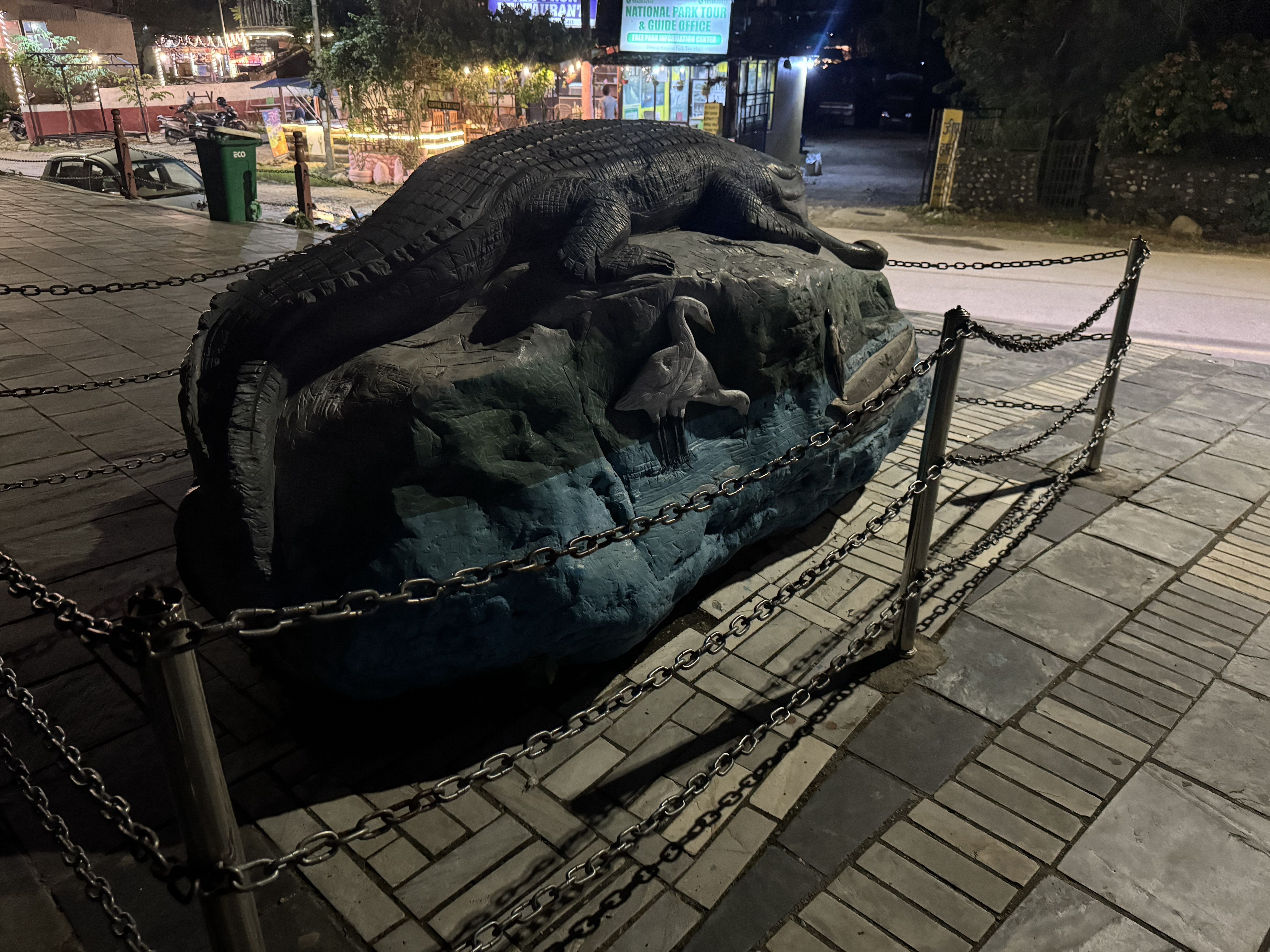 Dark crocodile sculpture on a painted rock outside a National Park Tour storefront at night.