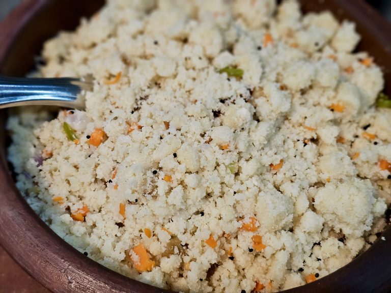 A close-up view of vegetable upma served in a traditional earthen bowl, showing its soft texture, carrots, green chilies, mustard seeds, and onions. Location: Ayamkudy, Kottayam, Kerala.