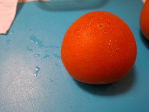 Tomato covered in water drops on a blue plastic cutting board.
