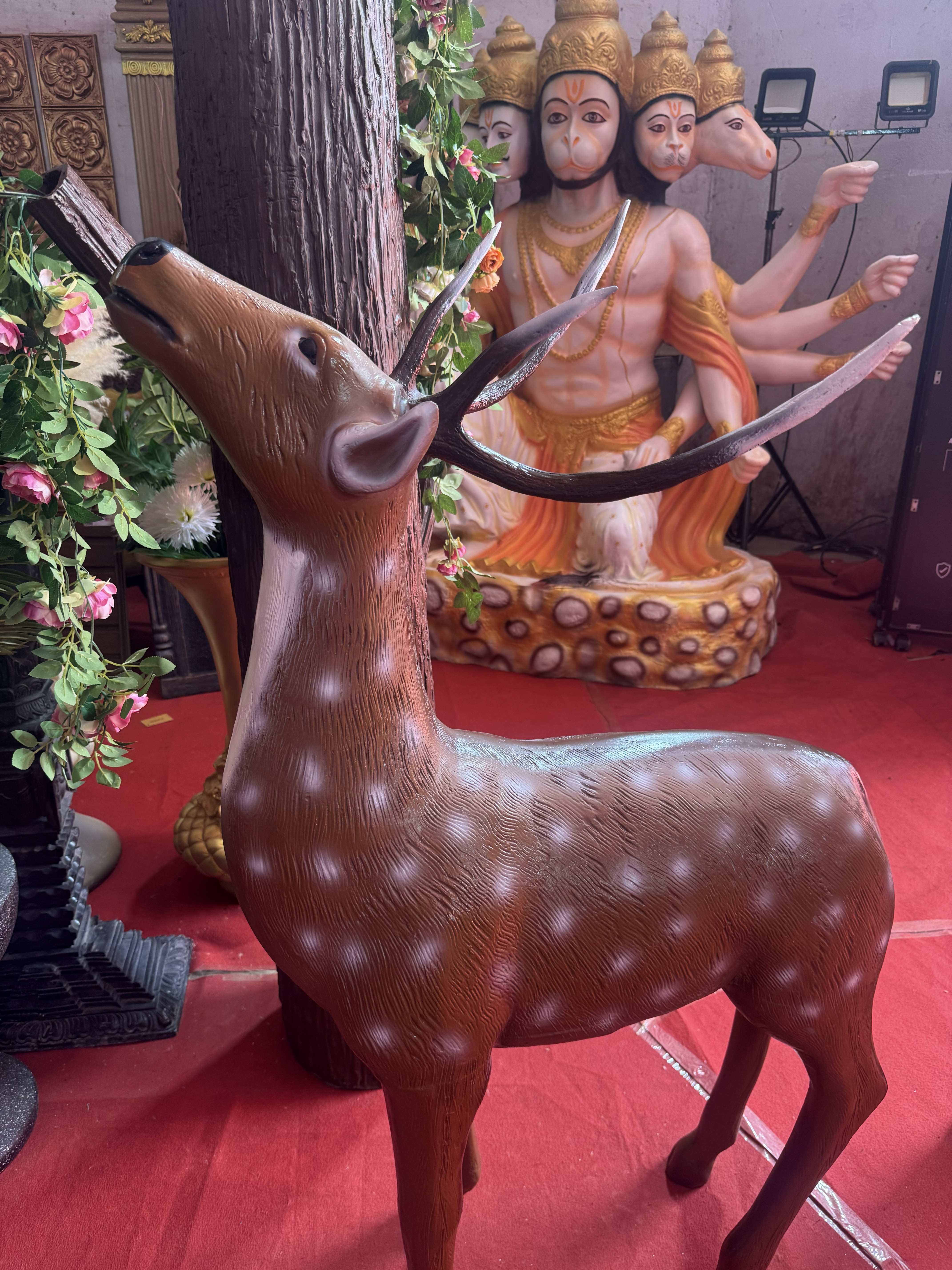 A brown spotted deer sculpture standing in front of a multi-faced Hindu deity statue (Panchamukhi Hanuman/Lord Brahma)