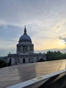 The stone dome of St Paul's Cathedral set against a warm sunset sky viewed from an elevated terrace in London.