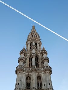 Intricate Brabantine Gothic spire of Brussels Town Hall reaching into a clear blue sky crossed diagonally by an airplane contrail.
