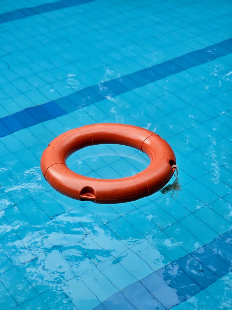 A life buoy floating on the blue water of a swimming pool, with lane markings and reflections visible around it. The contrasting colors create a strong composition. Location: Ayamkudy, Kottayam, Kerala.