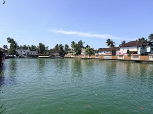 Kuttichira Pond in Kozhikode, surrounded by historic tiled-roof buildings and lush tropical greenery beneath a clear blue sky.