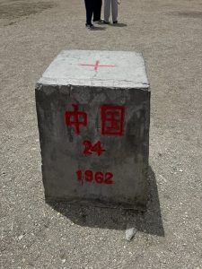 Close-up of international border pillar No. 24 marked “China,” with the year 1962, standing on dry gravel ground.