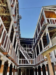 A wide, low-angle perspective looking up at the wooden balconies, staircases, and white railing corridors of a multi-story traditional mountain lodge or teahouse.