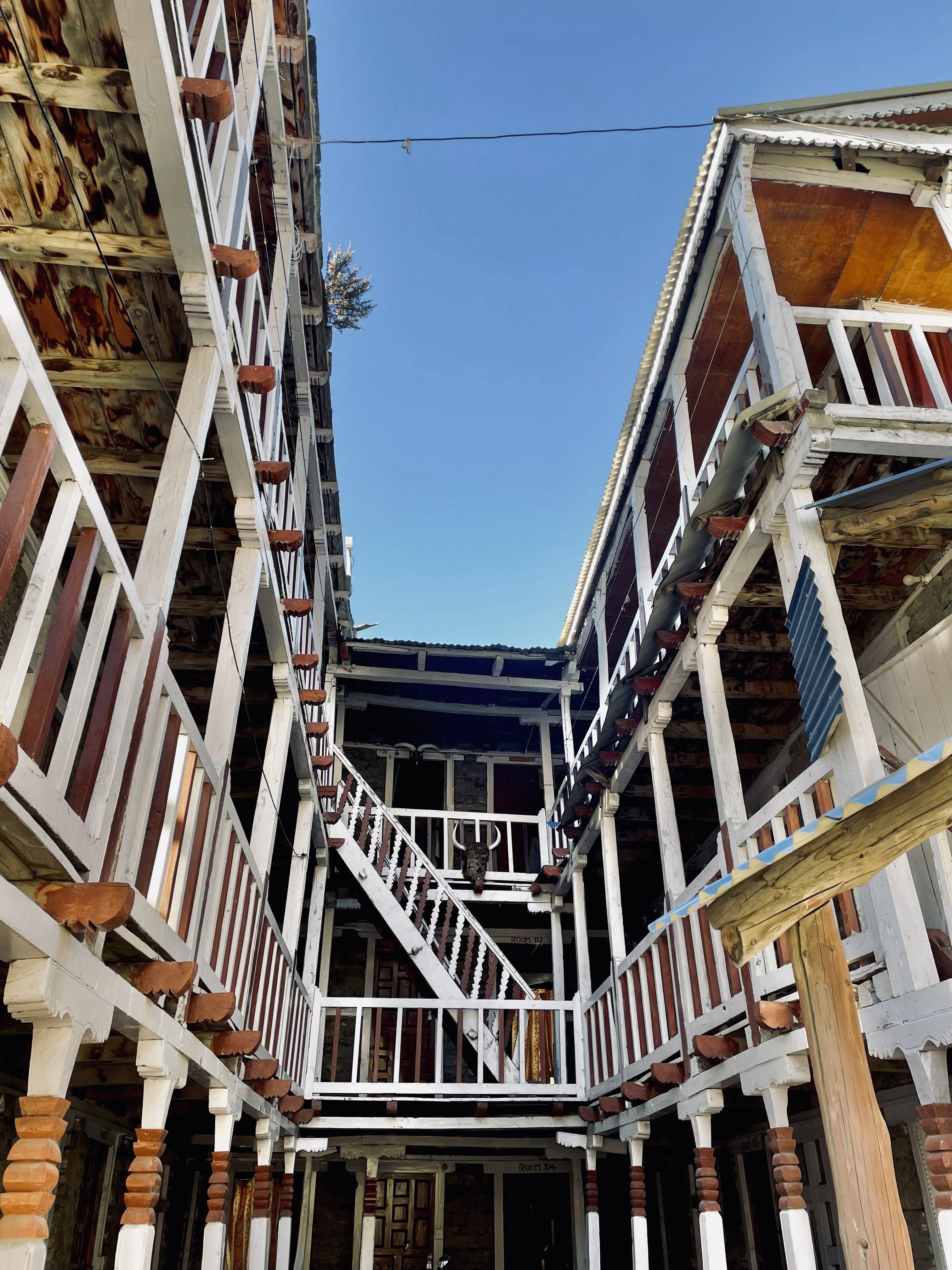 A wide, low-angle perspective looking up at the wooden balconies, staircases, and white railing corridors of a multi-story traditional mountain lodge or teahouse.