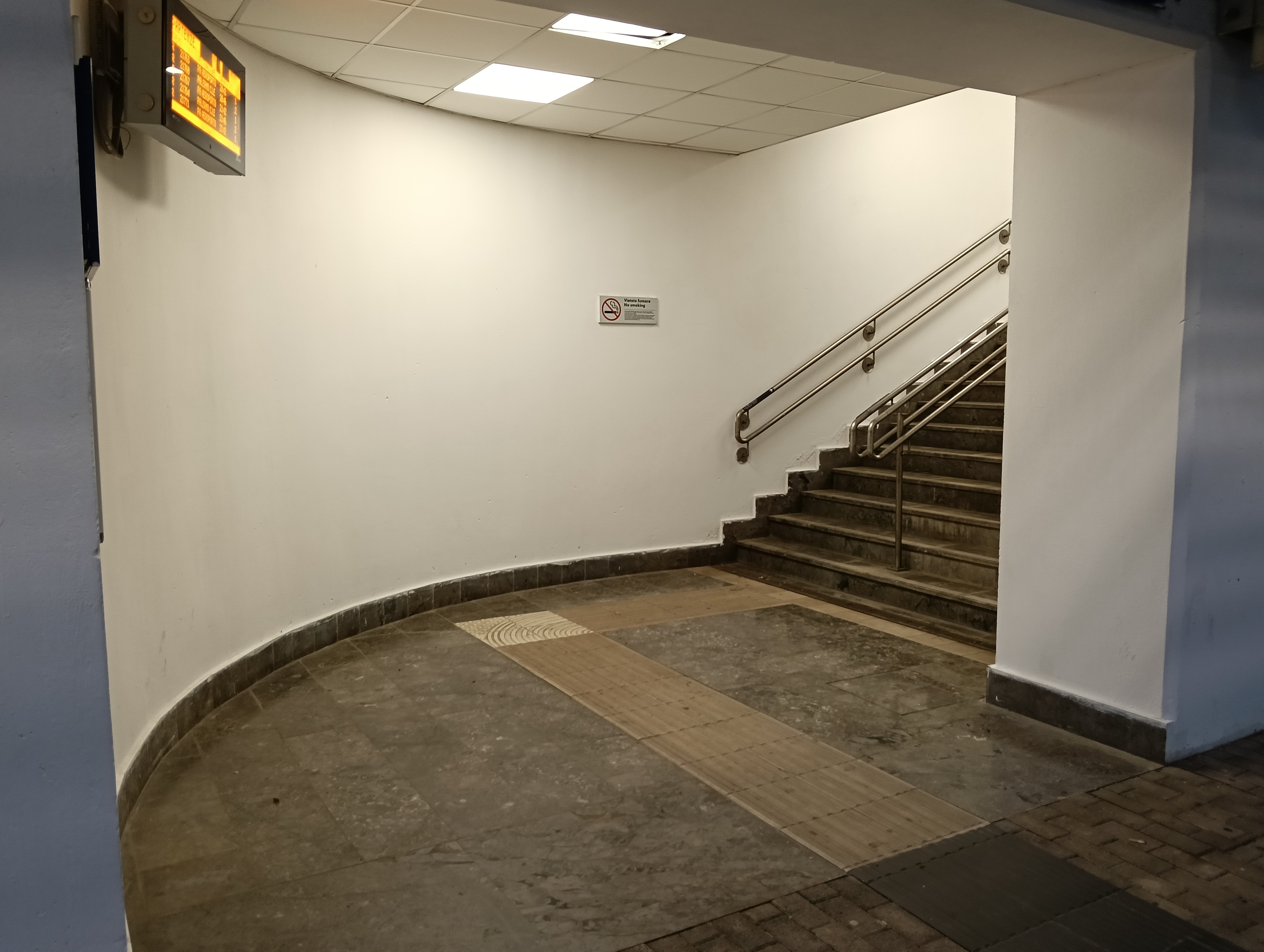 Corner of the train station stairs, featuring a departures screen and a smoking notice.
