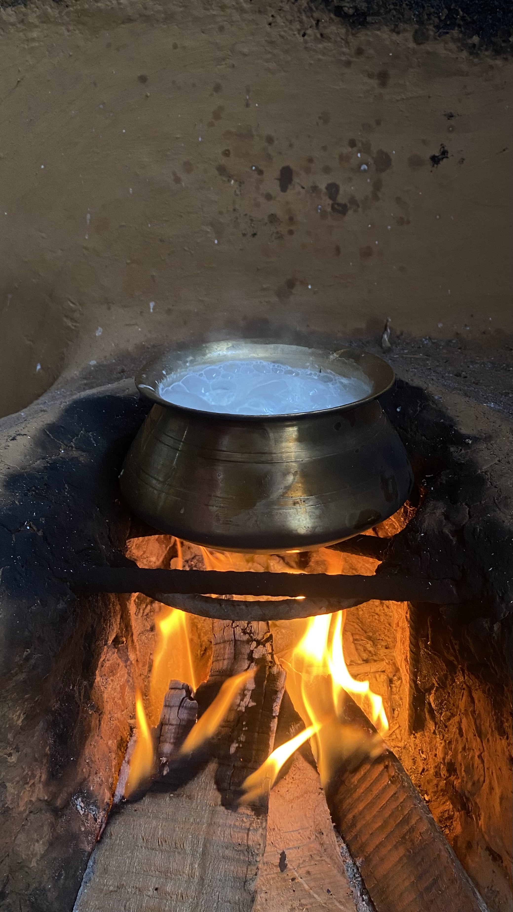 A traditional metal pot of milk heating over a wood fire in a rustic kitchen, capturing the warmth of traditional cooking.