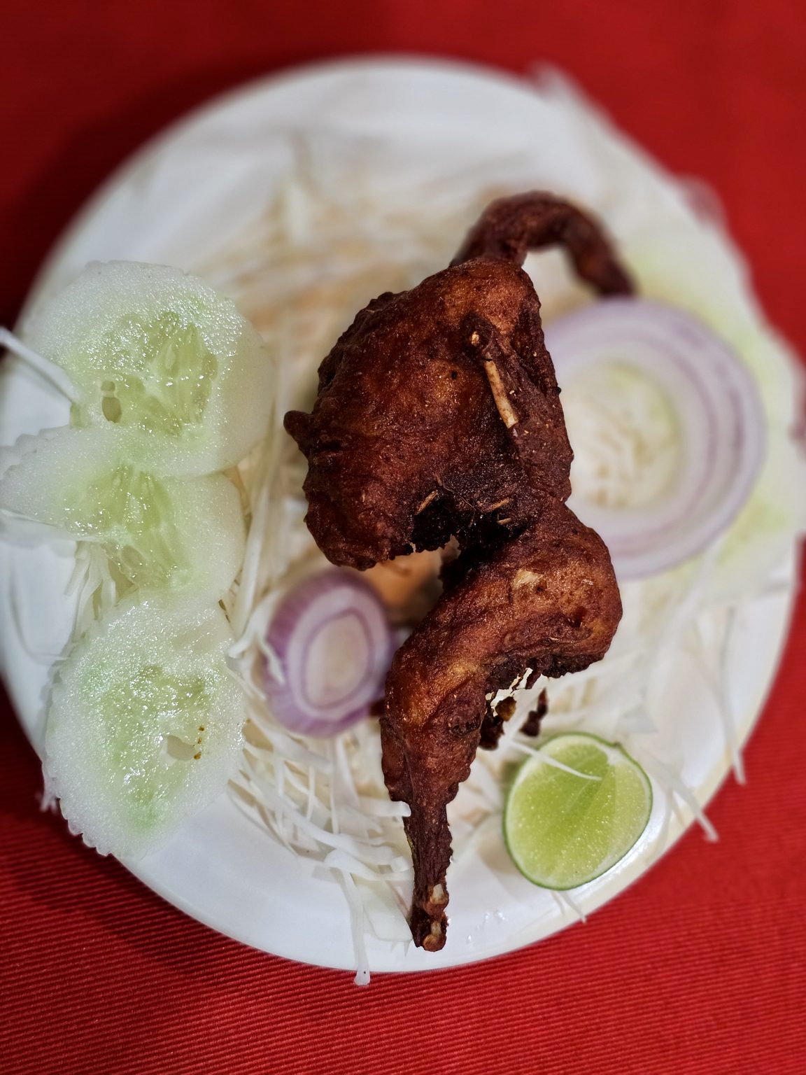 A plate of crispy Kaada Fry (deep-fried quail) is served with cucumber, onion, cabbage, and lime, creating a colorful, appetizing dish. Location: Ayamkudy, Kottayam, Kerala.