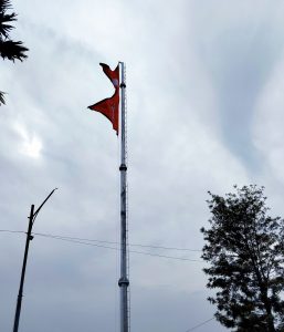 Nepalese flags flying from a tall flagpole against a cloudy sky, with a tree and utility pole nearby.
