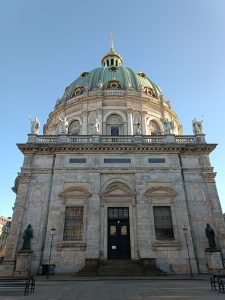 Front exterior view of Frederik's Church (Marble Church) in Copenhagen featuring its green copper dome, marble facade, and statues under a clear sky.