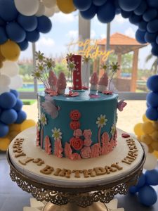 
A colorful birthday cake is displayed on an ornate silver stand. 