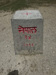 Close-up of an international border pillar marked “Nepal,” number 24, and year 2066 BS, standing on gravel ground.