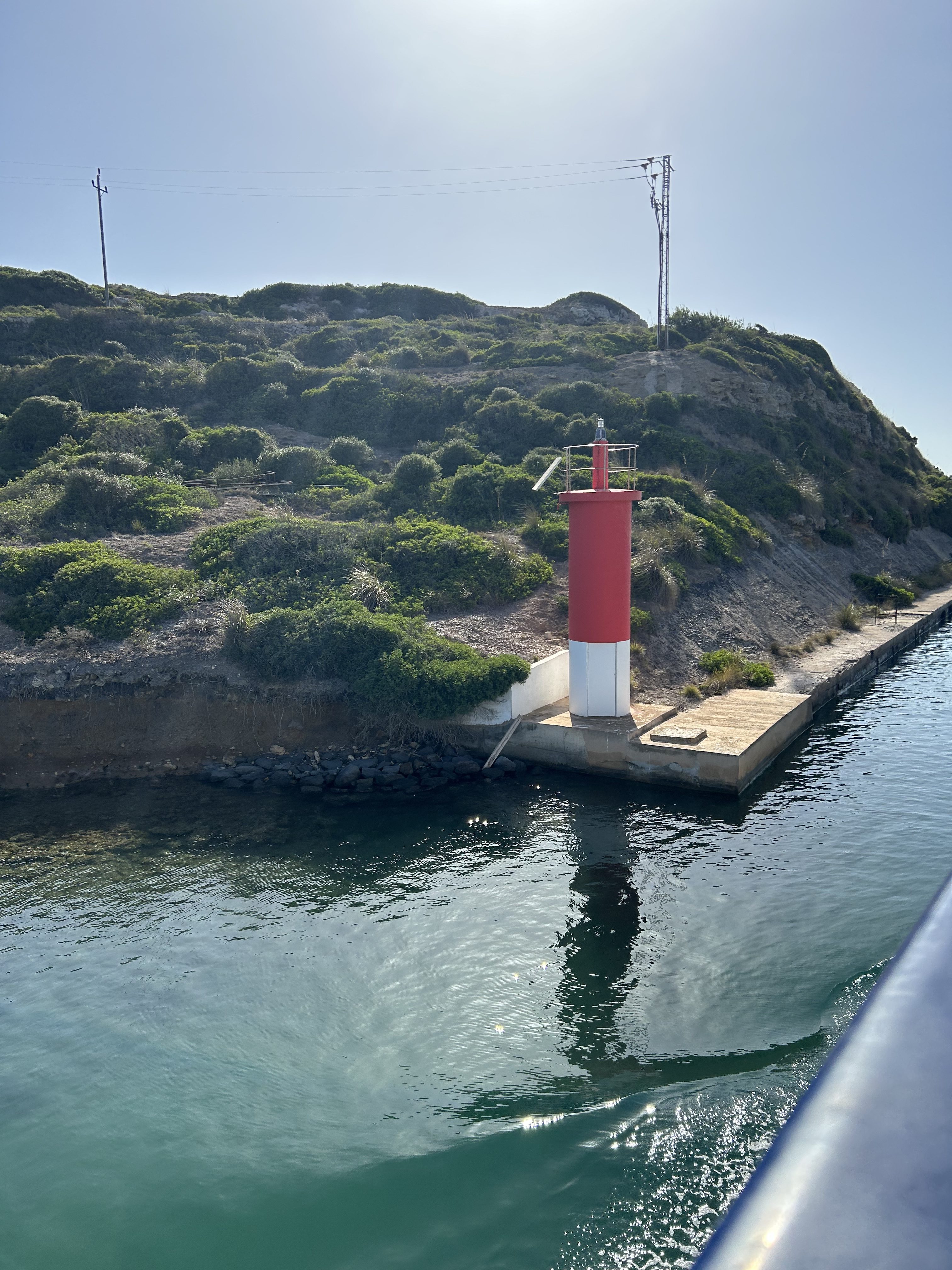 Small red and white lighthouse by the sea on a sunny day.