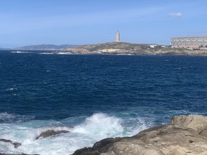 Atlantic Ocean waves crashing against the rocks, with the Tower of Hercules in the background.
