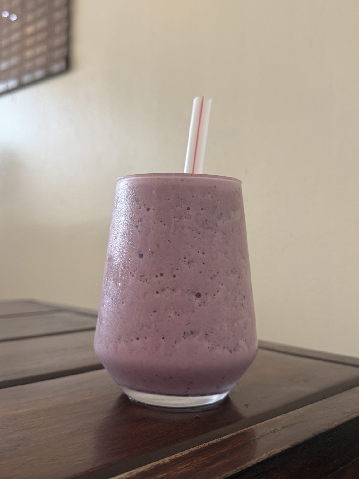 A smooth, rounded glass filled with a thick, creamy beverage in a vibrant shade of purple sits on a wooden table.