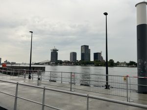 Amsterdam city skyline and the A'DAM Lookout tower across the river under a cloudy sky.