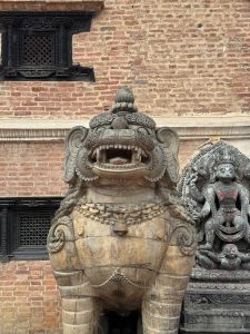 Large hand-carved stone lion guardian (Gaja Simha) in front of a traditional red brick wall and carved wooden window.