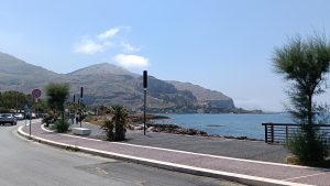 Different pathways and a winding road beside the sea, with a distant valley in the background.