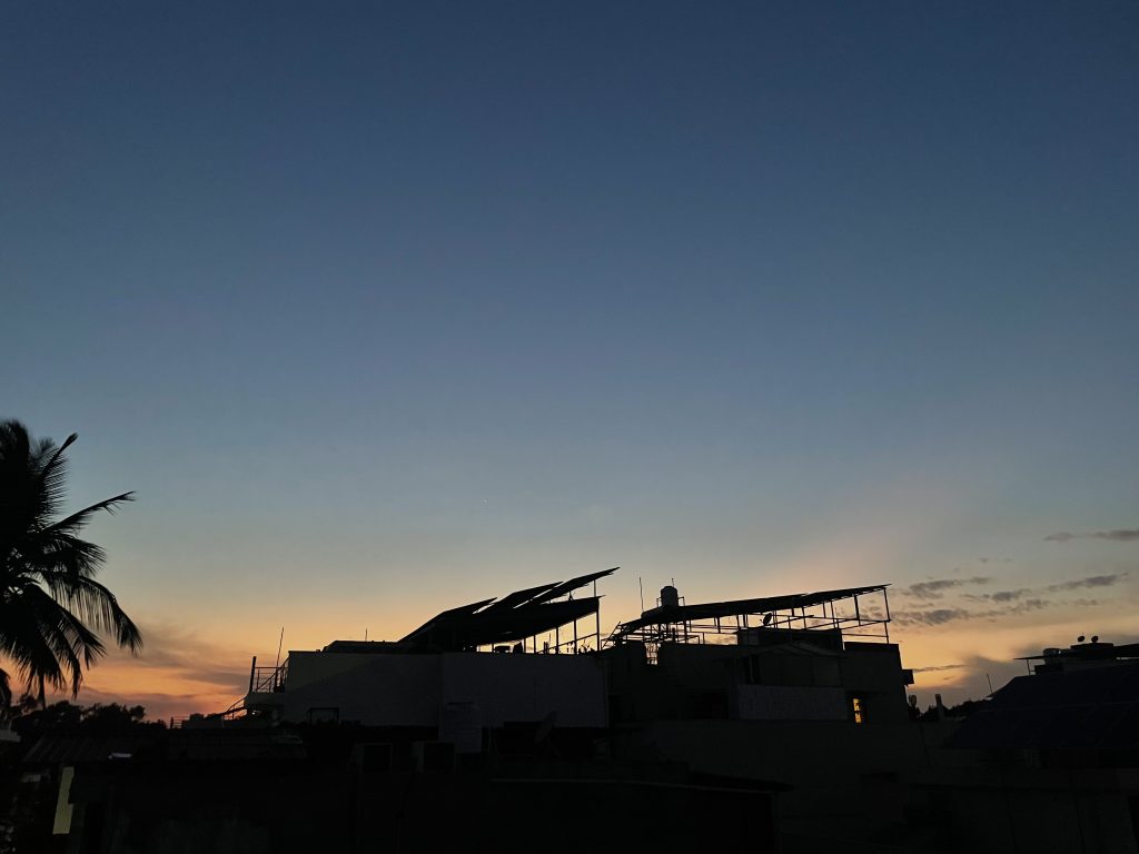 Sunset taking place while there’s one star in the sky, and the colour of the sky is turning orange and yellow. Trees and terrace of a house can also be seen alongwith.