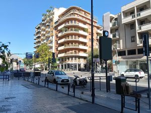 Road intersection at a modern city in a sunny day, including pathways, buildings, vehicles and the clear sky.