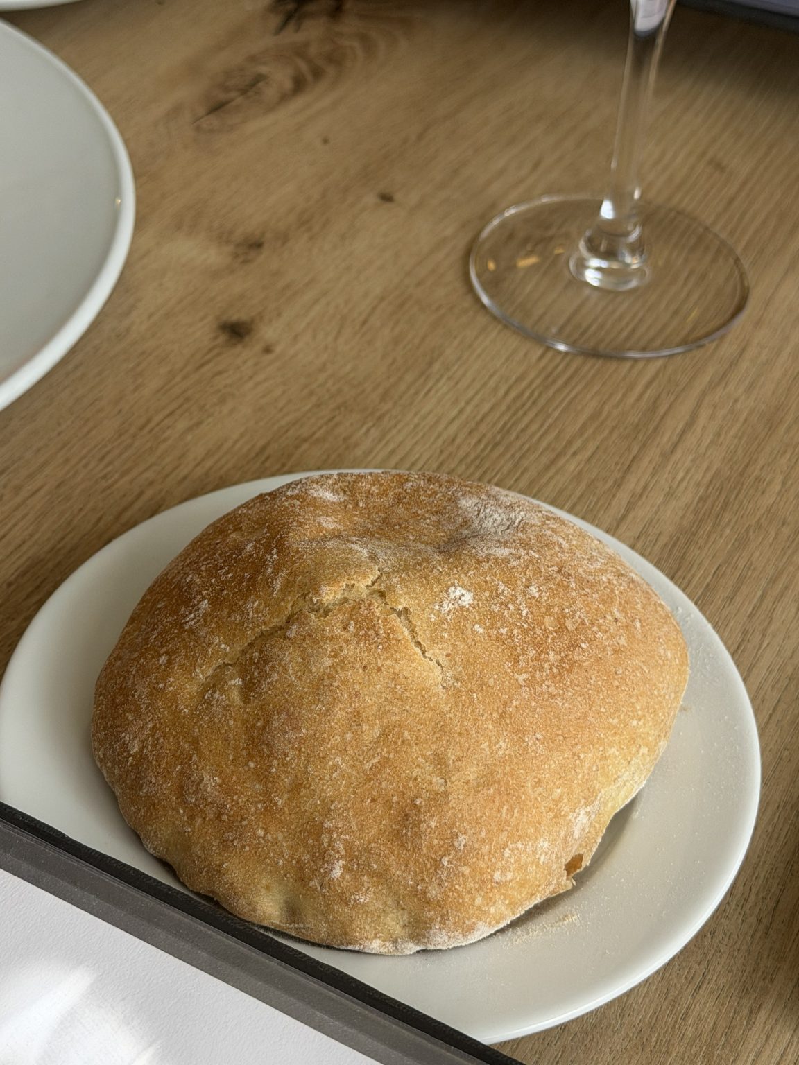 A crusty flour-dusted bread roll on a small white plate on a wooden table.