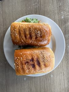 Two golden-brown sesame-seed sandwiches filled with lettuce and tomato slices on a white plate.