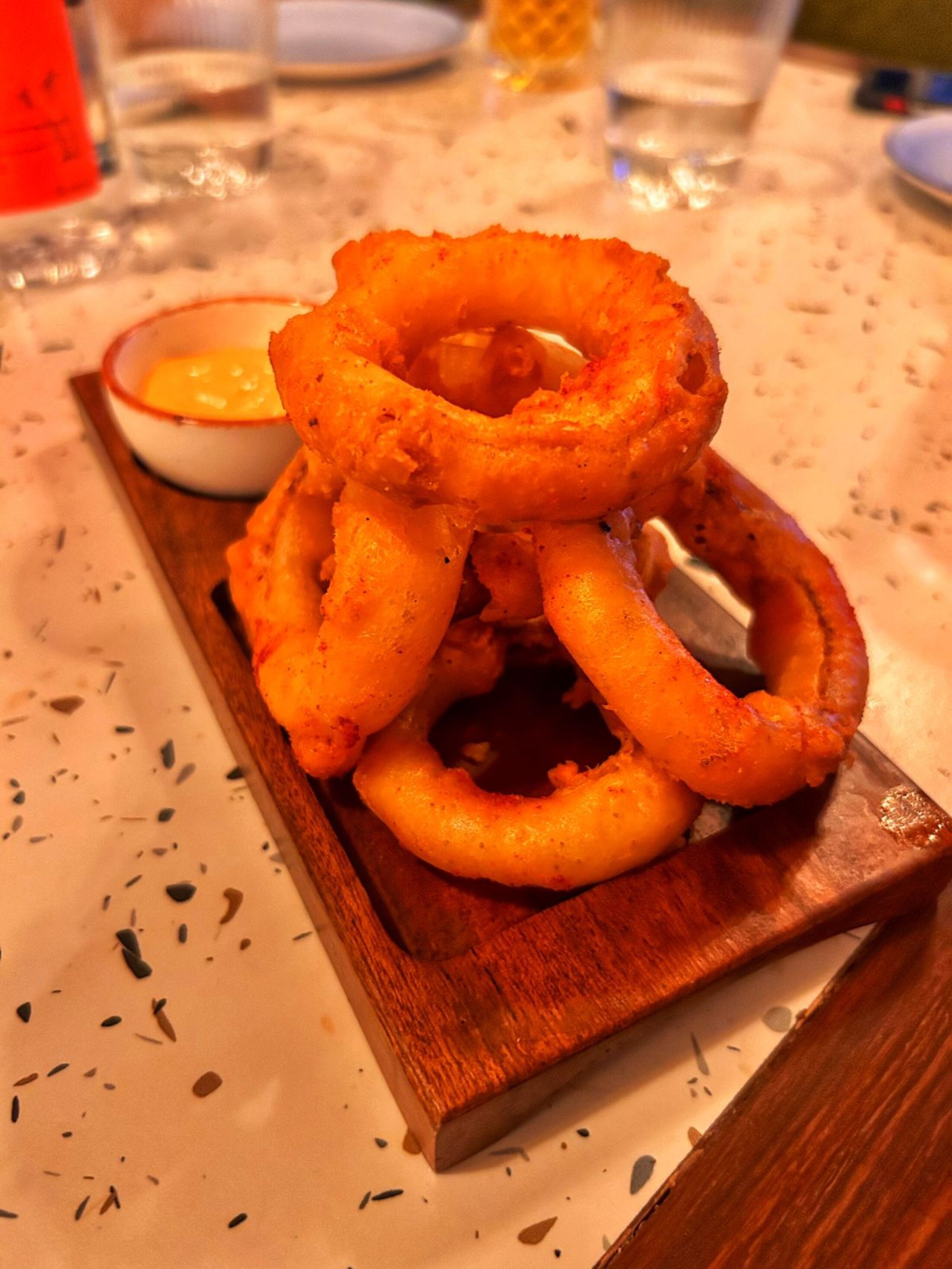 Onion rings served on a wooden serving tray with a small bowl of dipping sauce