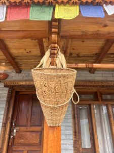 The image features a woven basket hanging from a wooden beam under a porch. 
