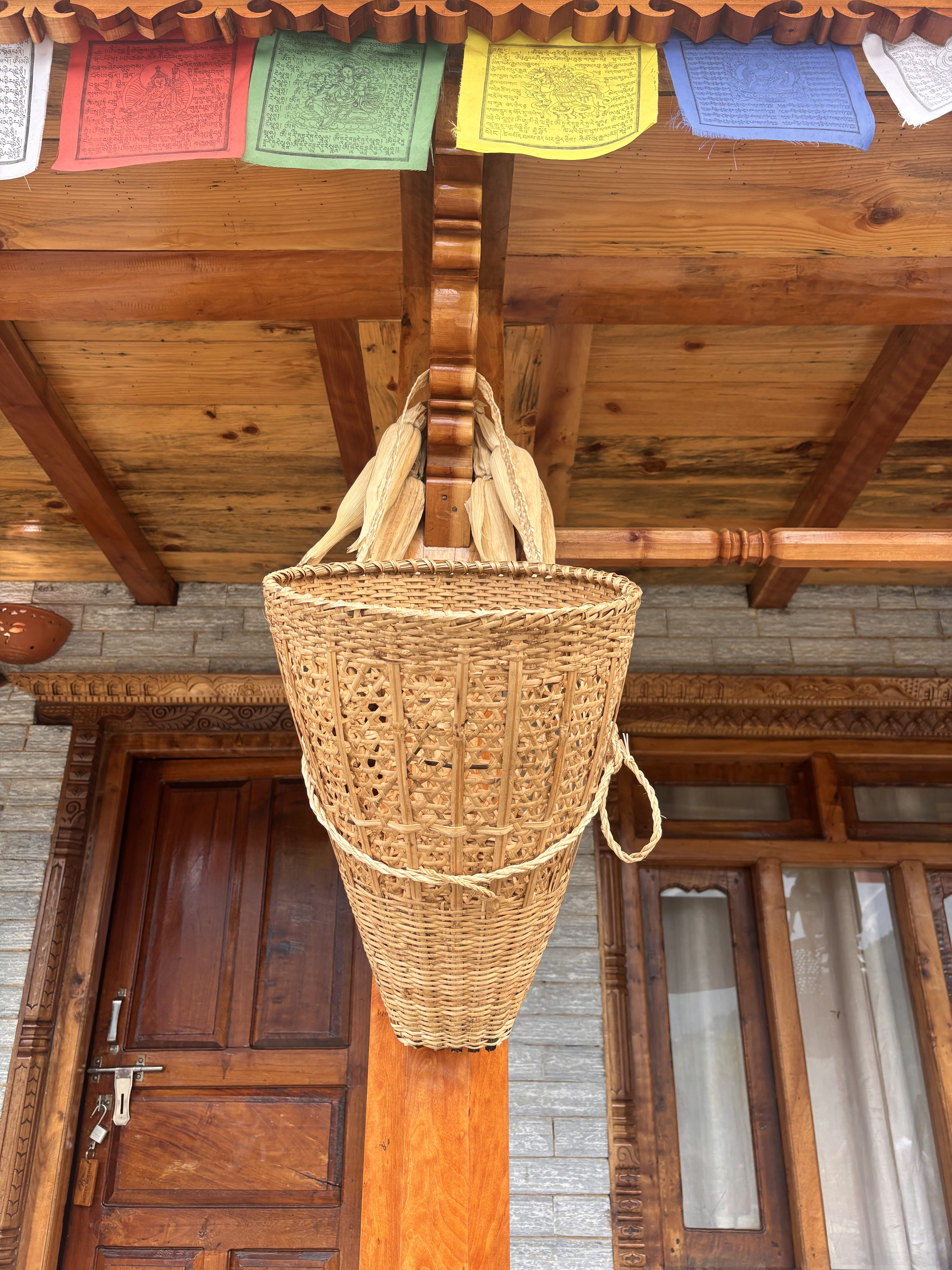 The image features a woven basket hanging from a wooden beam under a porch.