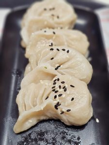 A close-up view of freshly prepared steamed dumplings arranged on a black plate. The soft folds, glossy texture, and black-and-white sesame seeds stand out beautifully against the dark background. Location: Kozhikode, Kerala.