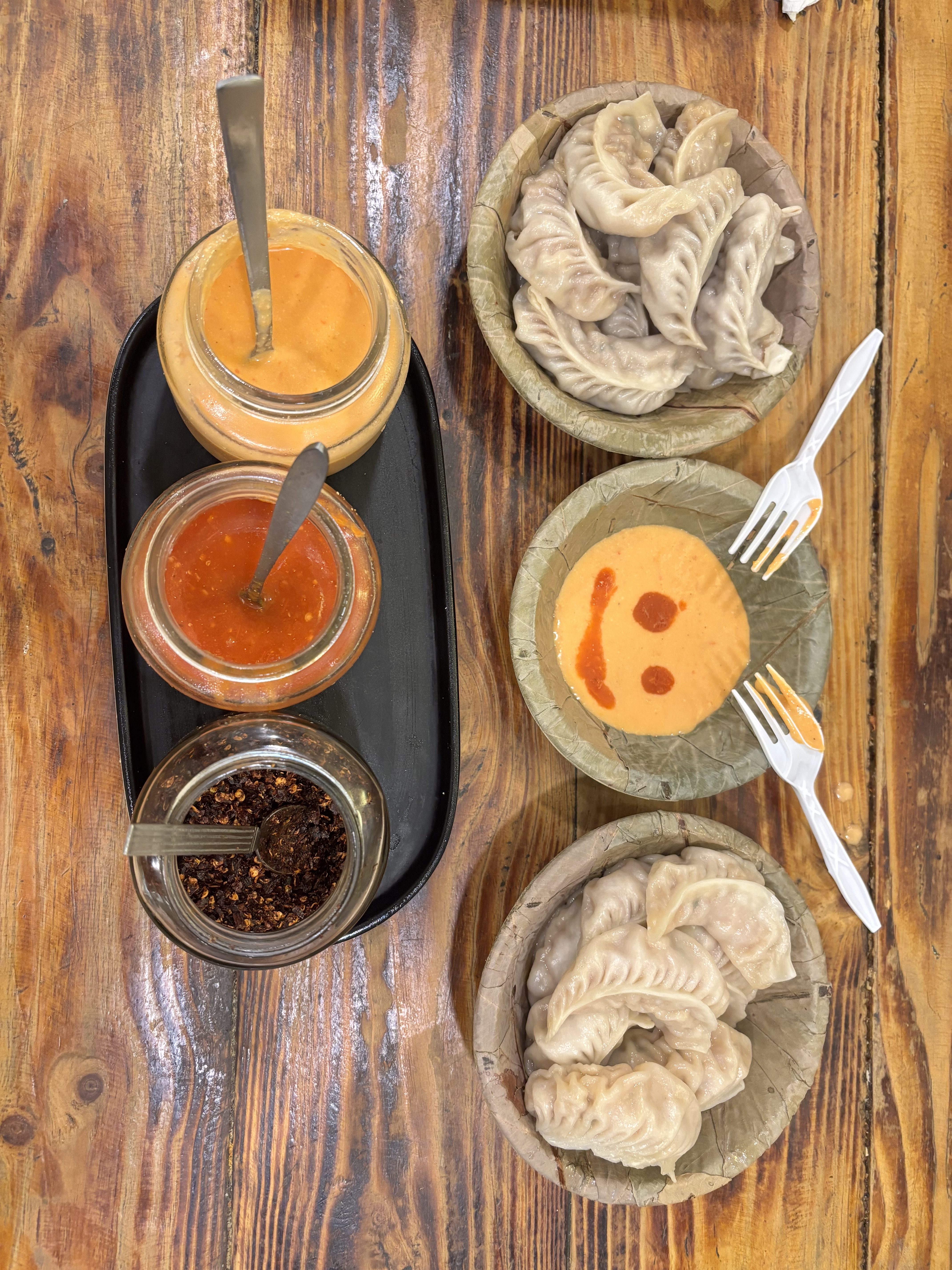 Dumplings, dipping sauces, and red pepper flakes served in palm leaf bowls on a wooden table.