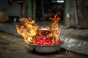 Religious offerings burning in a steel pan on a street in Vietnam.
