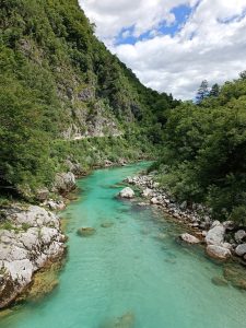 Turquoise river winding through a rocky mountain gorge surrounded by dense green forest under a cloudy sky.