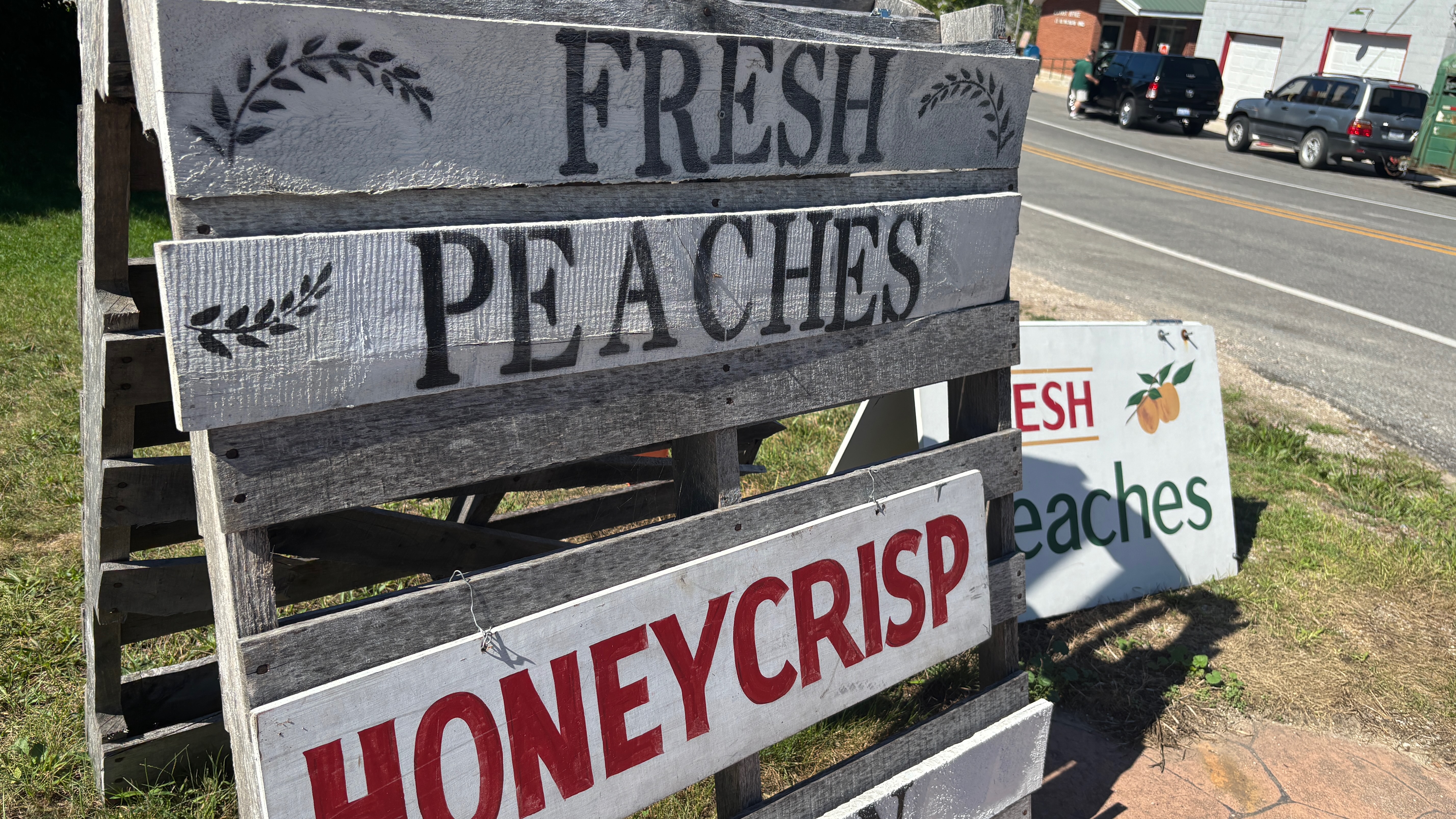 A rough wooden sign advertising Fresh Peaches, and Honeycrisp apples.