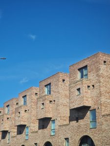 Repetitive geometric architectural pattern of modern red brick residential units and balconies against a vibrant blue sky.