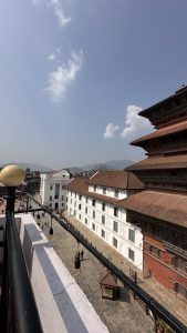 People walking alongside a large white building which is next to a tall pagoda. Basantapur, Nepal
