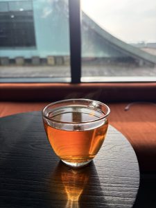 A clear glass filled with black tea sits on a dark round wooden table, illuminated by warm sunlight from a window