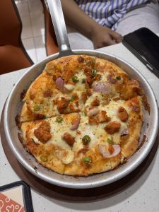 Chicken pizza topped with melted cheese, red onion, and green chilies on a metal pan.
