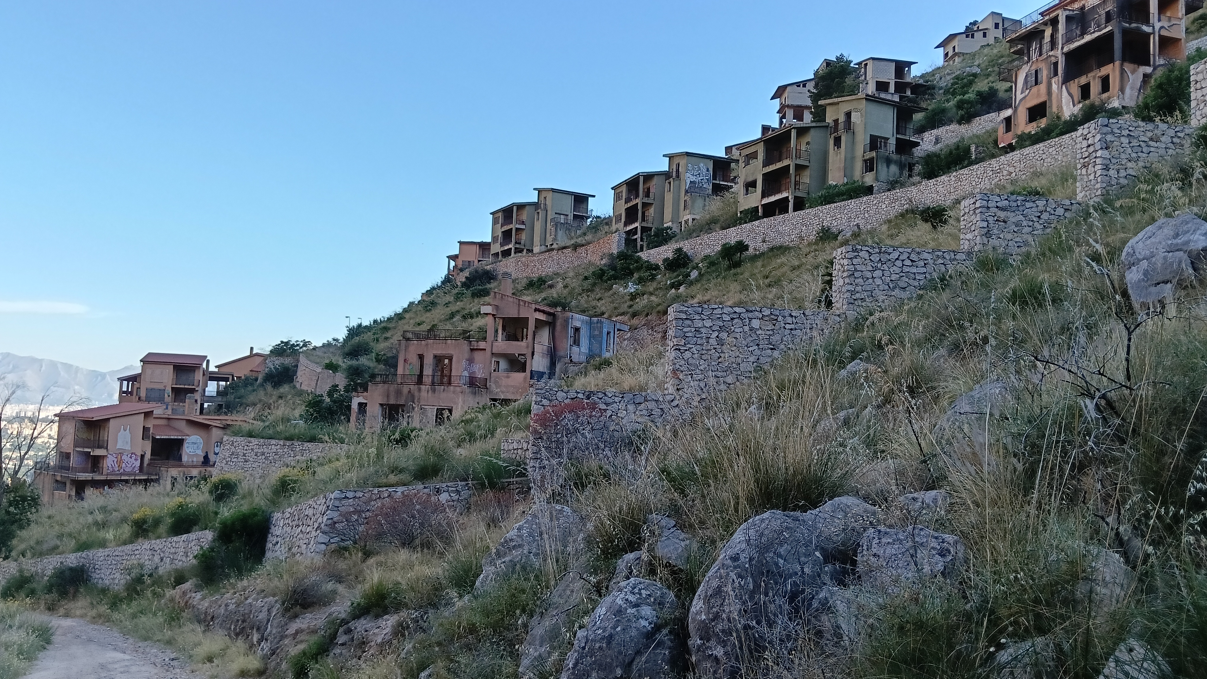 Many abandoned houses and walls over a green valley.