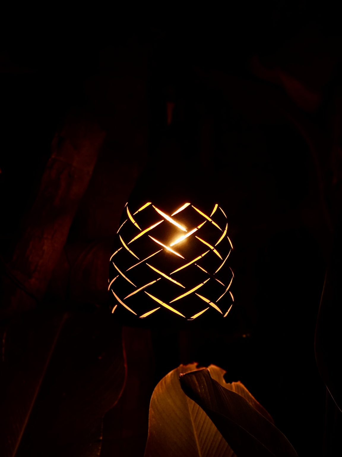 A glowing decorative lamp with an intricate woven pattern creates a warm, artistic scene against a dark background. The strong contrast beautifully highlights the light and surrounding shapes. Location: Edavannappara, Malappuram, Kerala