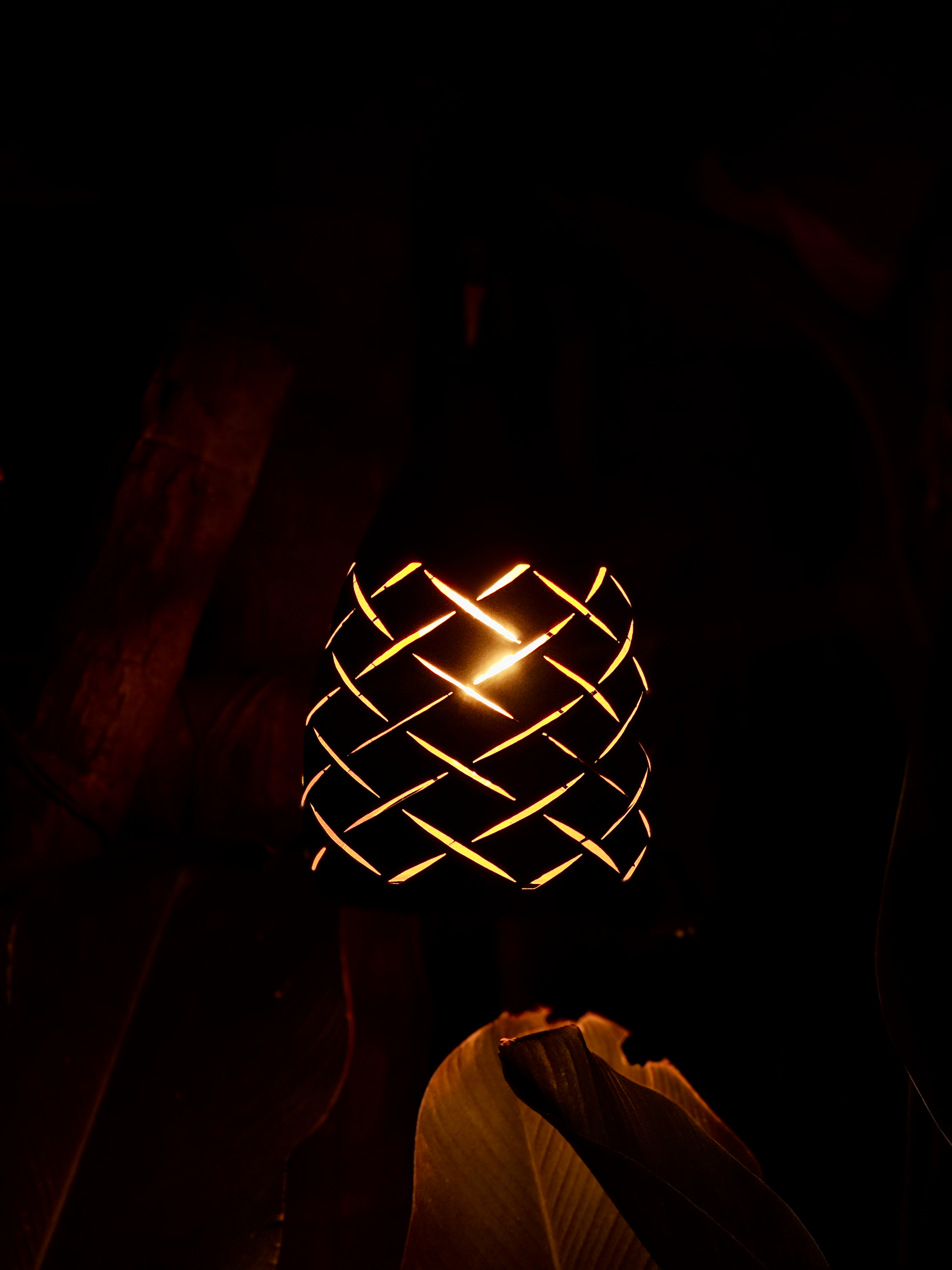 A glowing decorative lamp with an intricate woven pattern creates a warm, artistic scene against a dark background. The strong contrast beautifully highlights the light and surrounding shapes. Location: Edavannappara, Malappuram, Kerala