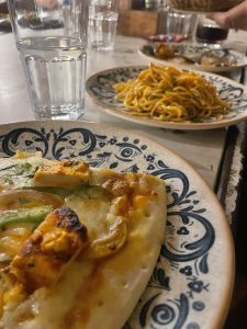 Pizza with cottage cheese (paneer), capsicum, onion and cheese over it, along with veg chilly garlic noodles kept on the next dish, while a glass of water sits on the side.